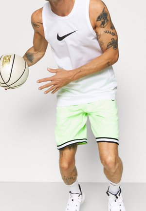Débardeur Nike sans manches blanc avec logo noir, associé à un short vert fluo avec des bordures noires, et un ballon de basket à la main.