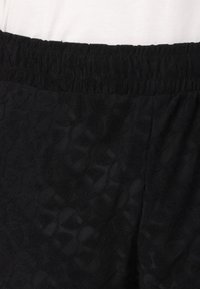 Tejido negro texturizado con un patrón sutil, que cuenta con una cinturilla elástica. La vista en primer plano se centra en el material y los detalles del diseño.