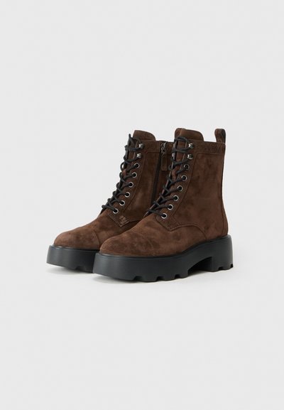 Stivaletti in suede marrone con lacci, cerniera laterale e suole in gomma nera spessa su uno sfondo semplice.