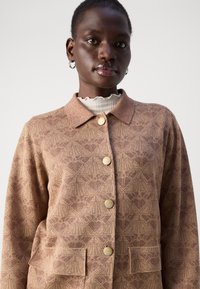 Braun gemusterte Jacke mit kragenförmigem Ausschnitt, metallischen Knöpfen und zwei vorderen Taschen. Verfügt über ein dezentes strukturiertes Design.
