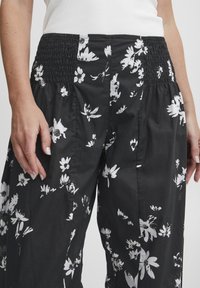 Svarta byxor med blommönster, smockad midja och lös passform. Har vita blommor av olika former och storlekar på tyget.