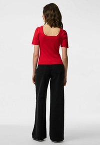Top rosso aderente con maniche a sbuffo corte e scollatura quadrata, abbinato a pantaloni neri a gamba larga con vita alta. Tessuto liscio, dettagli minimi.