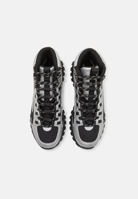 Høye sneakers med en svart og sølvfarget fargepalett, teksturerte overflater, tykke gummisåler og kontrastsnøringer.