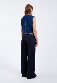 Top corto de denim con corte recto y cremallera en la parte trasera; combinado con pantalones de denim oscuros de pierna ancha que cuentan con bolsillos traseros y una etiqueta de cuero.