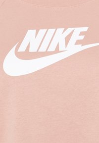 Jasnoróżowa bluza z dużym białym logo Nike, o gładkiej fakturze i klasycznym, okrągłym dekolcie.