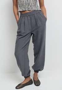 Graue, locker sitzende Hose mit elastischem Bund und Bündchen. Hergestellt aus leichtem Stoff, mit Seitentaschen und strukturierter Oberfläche.