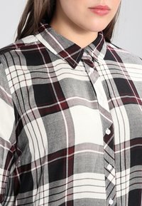 Skjorte med knapper og et sort, hvidt og bordeaux ternet mønster. Fremstillet af let stof med klassisk krave og knapper foran.