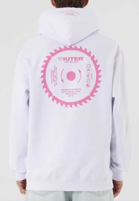 Felpa bianca con cappuccio e grafica circolare rosa che presenta un design di sega sul retro. Il materiale sembra morbido; presenta un cappuccio con cordino e polsini a coste.
