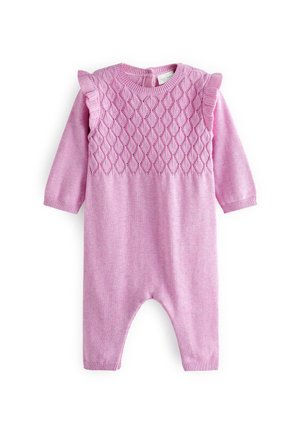Baby iført en lyserød strikket dragt liggende på en hvid overflade ved siden af en lille beige tøjdyrmus.