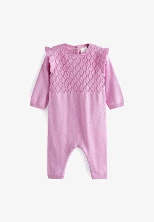 Baby draagt een roze gebreide outfit en ligt op een wit oppervlak naast een klein beige knuffelmuisje.