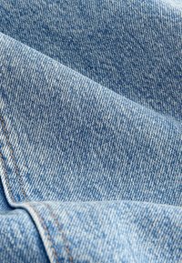 Gros plan d'un tissu en denim bleu clair montrant une couture diagonale et une texture de tissage détaillée.