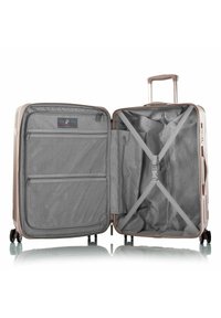 Valigia rigida color oro rosa con interno grigio, tasche in rete, cinghie incrociate e manico retrattile. Quattro ruote per la mobilità.