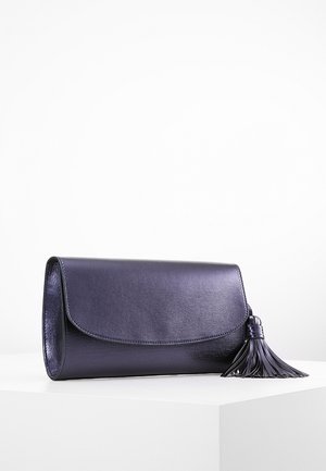 Bolso de mano de cuero morado oscuro con solapa redondeada y un gran borlón a juego en el lado derecho, colocado sobre una superficie blanca.