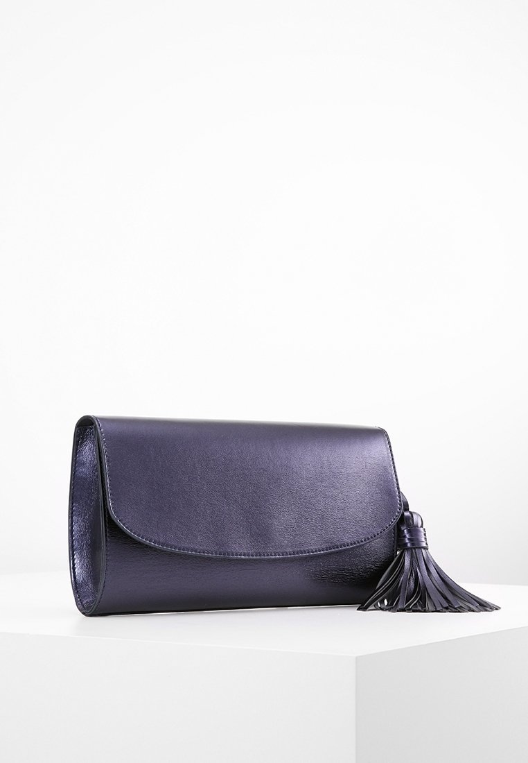 Pochette en cuir violet foncé avec rabat arrondi et un grand pompon assorti sur le côté droit, posée sur une surface blanche.