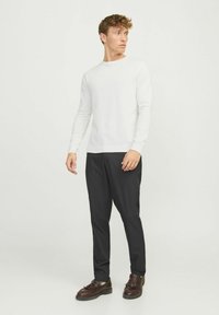 Witte gebreide trui met lange mouwen, zwarte slim-fit broek en bruine schoenen. Eenvoudig ontwerp, gladde textuur en aansluitende silhoette.
