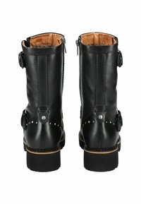 Botas de tobillo de cuero negro con un acabado suave, tachuelas decorativas, cremalleras laterales y un interior acolchado marrón. Suelas de goma planas.