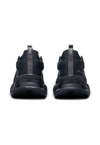 Schwarze Sportschuhe mit schlankem Design, strukturiertem Mesh-Obermaterial, gepolstertem Fersenbereich und Gummisohle. Mit einer Zuglasche an der Rückseite für ein einfaches Anziehen.