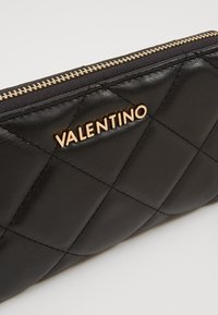 Černá prošívaná kožená peněženka se zlatým logem "Valentino", se zlatým zipem a texturovaným diamatovým vzorem na povrchu.