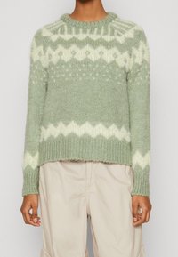 Jasnozielony sweter dziany z okrągłym dekoltem, ozdobiony białym wzorem w zygzak i teksturowanymi rękawami, krótki krój, miękki materiał.