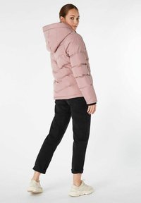 Jasnoróżowa kurtka puchowa z poziomym przeszyciem i kapturem, zestawiona z czarnymi spodniami i jasnymi sneakersami. Gładka tekstura, casualowy design.