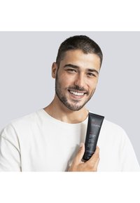 Czarna tuba żelu do oczyszczania Collistar, 125 ml, z czerwonym i białym tekstem. Mężczyzna trzyma tubę, ubrany w beżowy t-shirt na jasnoszarym tle.