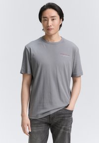 Grå bomulds t-shirt med korte ærmer, der har et lille rødt logo på brystet. Stoffet ser blødt og letvægts ud.