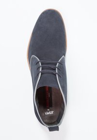 Chaussure en daim bleu foncé avec un bout rond, des lacets gris et une semelle en caoutchouc marron. Présente une texture lisse et un bord contrastant subtil.