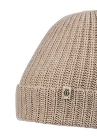 Beige knitted wool beanie with a folded cuff and a small rectangular tag featuring a black emblem.