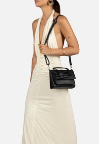 Borsa nera con motivo coccodrillo, dotata di manico superiore e tracolla regolabile. Vestito halter beige in satin con dettagli arricciati.