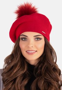 Berretto lavorato a maglia rosso con un grande pon-pon soffice in cima. Presenta una texture liscia e un sottile accento metallico sul lato.