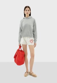 Grijze sweatshirt met een capuchon, witte shorts met een rood hartontwerp, rode tote bag en beige instappers. Eenvoudige en casual outfit.