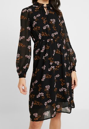Czarna sukienka do kolan z długimi przezroczystymi rękawami, różowo-brązowym kwiatowym wzorem, talią podkreśloną paskiem oraz dekoltem z wycięciem na kokardę.