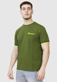T-shirt verde a maniche corte con scollatura rotonda, caratterizzato da una tasca sul petto e dettagli in giallo neon sulla tasca e sulle maniche.