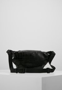 Černá kabelka s krokodýlím vzorem a hladkou texturou, vybavená nastavitelným popruhem a plastovou sponou, navržená v kompaktním tvaru.