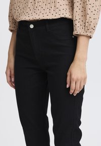 Jeans en denim noir à coupe étroite, avec des poches avant, une fermeture à bouton en métal et des coutures discrètes le long des côtés.