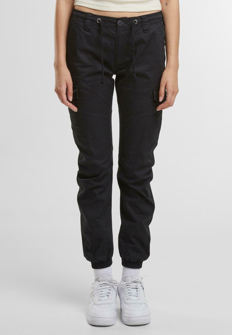 Sorte cargobukser med elastiske manchetter, snortræk i livet, sidelommer og en løs pasform, parret med hvide sneakers og ankelstrømper.