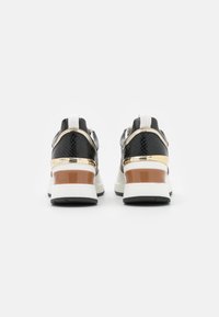 Svarta sneakers med en texturerad ovandel, metalliska guldaccenter och en kraftig vit sula med en brun insats. Bakifrån som visar design detaljer.