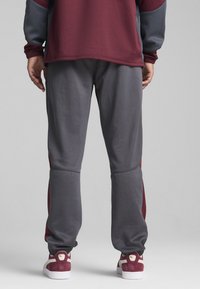 Maron og grå atletiske joggere med en afslappet pasform, der har sidepaneler i maron og afsluttede ankler. Udstyret med røde og hvide sneakers.