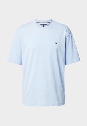 Hellblaues T-Shirt mit Rundhalsausschnitt und kurzen Ärmeln, mit kleinem Tommy Hilfiger Logo auf der linken Brust vor einfarbigem Hintergrund.