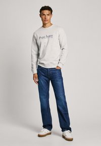Sivi dukserica s logom "Pepe Jeans", u kombinaciji s tamnoplavim trapericama i bijelim tenisicama. Ima okrugli izrez i rebraste manšete.