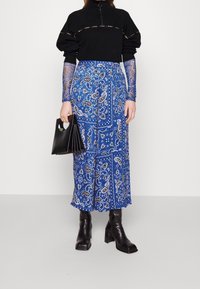 Top negro con cremallera y mangas abullonadas combinado con una falda culotte de patrón azul y botas negras hasta el tobillo. Bolso negro con asa troquelada.