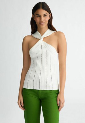 Balta halter top ar pagrieztu kakla izgriezumu, ribota tekstūra un vertikālām svītrām. Apvienots ar zaļām biksēm, izceļot krāsu kontrastu.