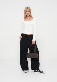 Witte lange mouwen top, zwarte brede broek, donkere handtas en zwarte sneakers. Eenvoudig ontwerp, casual pasvorm en soepele texturen.