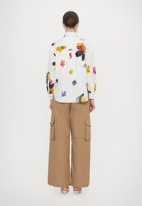 Floral printed white shirt with long sleeves paired with beige wide-leg cargo pants, featuring side pockets and a relaxed fit.