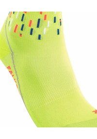 Neon-gelbe Socke mit geribbelter Textur, gepunktetem Muster in Rot, Blau und weißen Akzenten, mit reflektierenden grauen Details an der Seite.