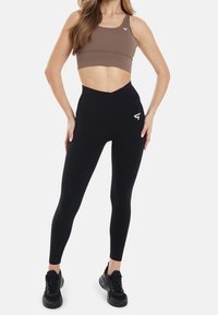 Brun sportstopp med kort ärm, ihopparad med högmidjade svarta leggings i elastiskt material, med en logotyp på sidan och en slank design.
