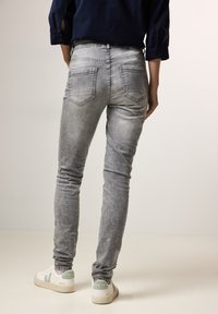 Jeans gris ajustados con un aspecto desgastado, cinco bolsillos y costuras minimalistas, combinados con zapatillas blancas con detalles verdes.
