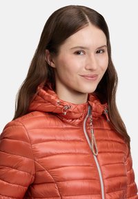 Polstret, lynlåslukket jakke i en livlig orange nuance. Udstyret med hættesnor, blank finish og ribbet tekstur i et quiltet design.