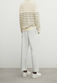 Pantalon blanc à jambe large associé à un pull crème à rayures, avec des rayures horizontales noires et un ourlet côtelé, complété par des baskets blanches.