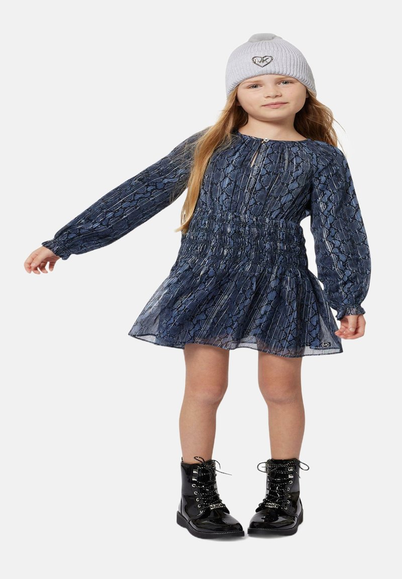 Robe à imprimé serpent bleu avec des manches longues, taille smockée et jupe évasée. Bottes noires à lacets. Bonnet en tricot gris avec un détail de cœur brodé.